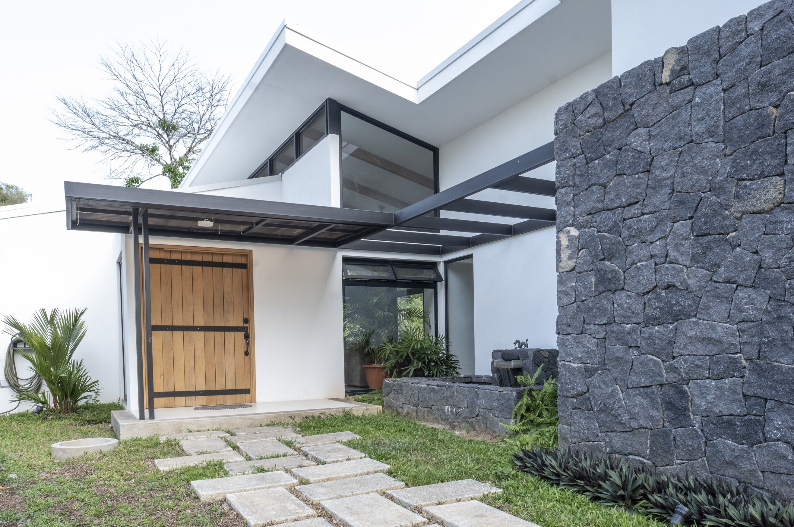 A modern house with a stone wall, a wooden door, and a glass door.