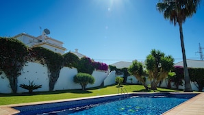 Uma piscina com bordas revestidas, rodeada por um gramado bem cuidado e diversas plantas.