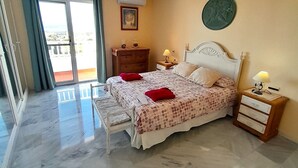 Quarto com cama, mesas de cabeceira, cômoda, um quadro e vista pela janela.