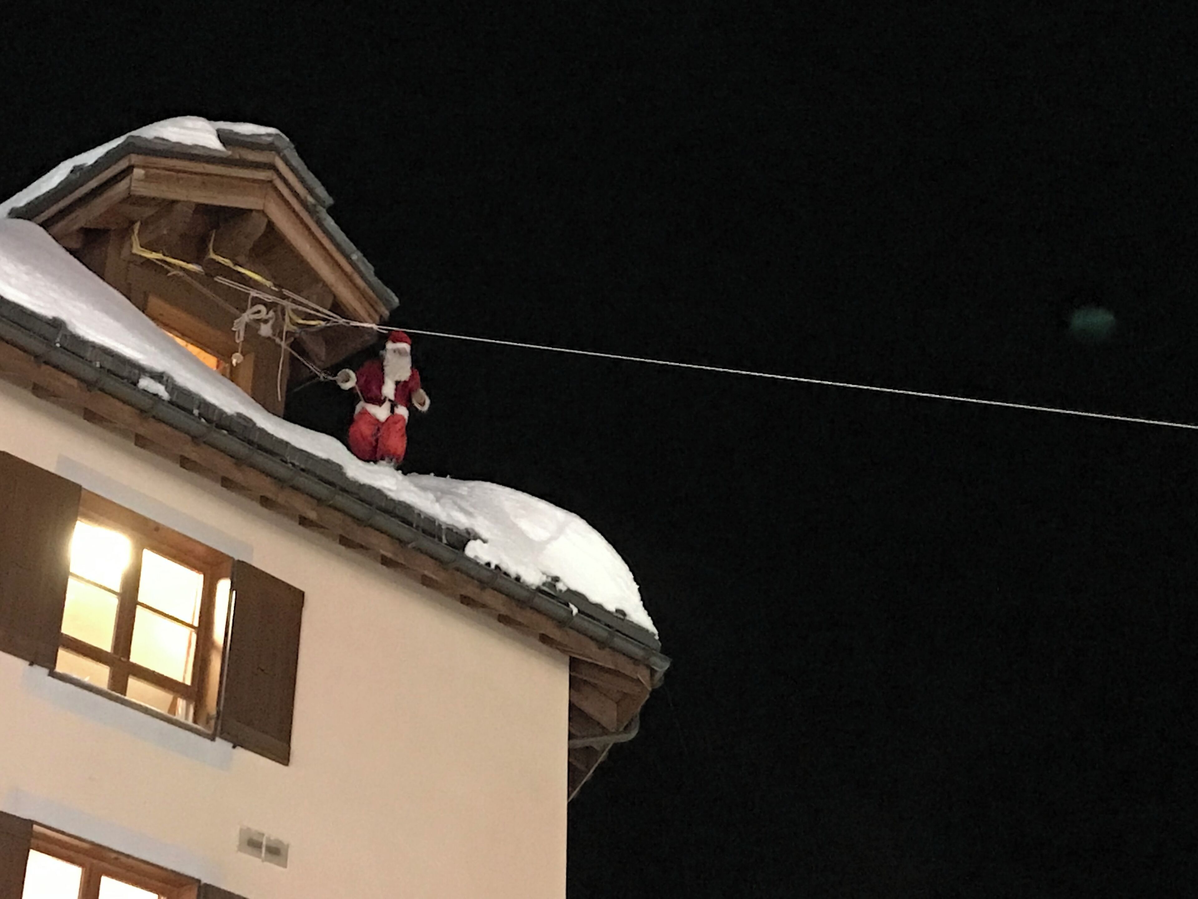 Un edificio con tejado cubierto de nieve y una figura que se asemeja a Papá Noel en el tejado.