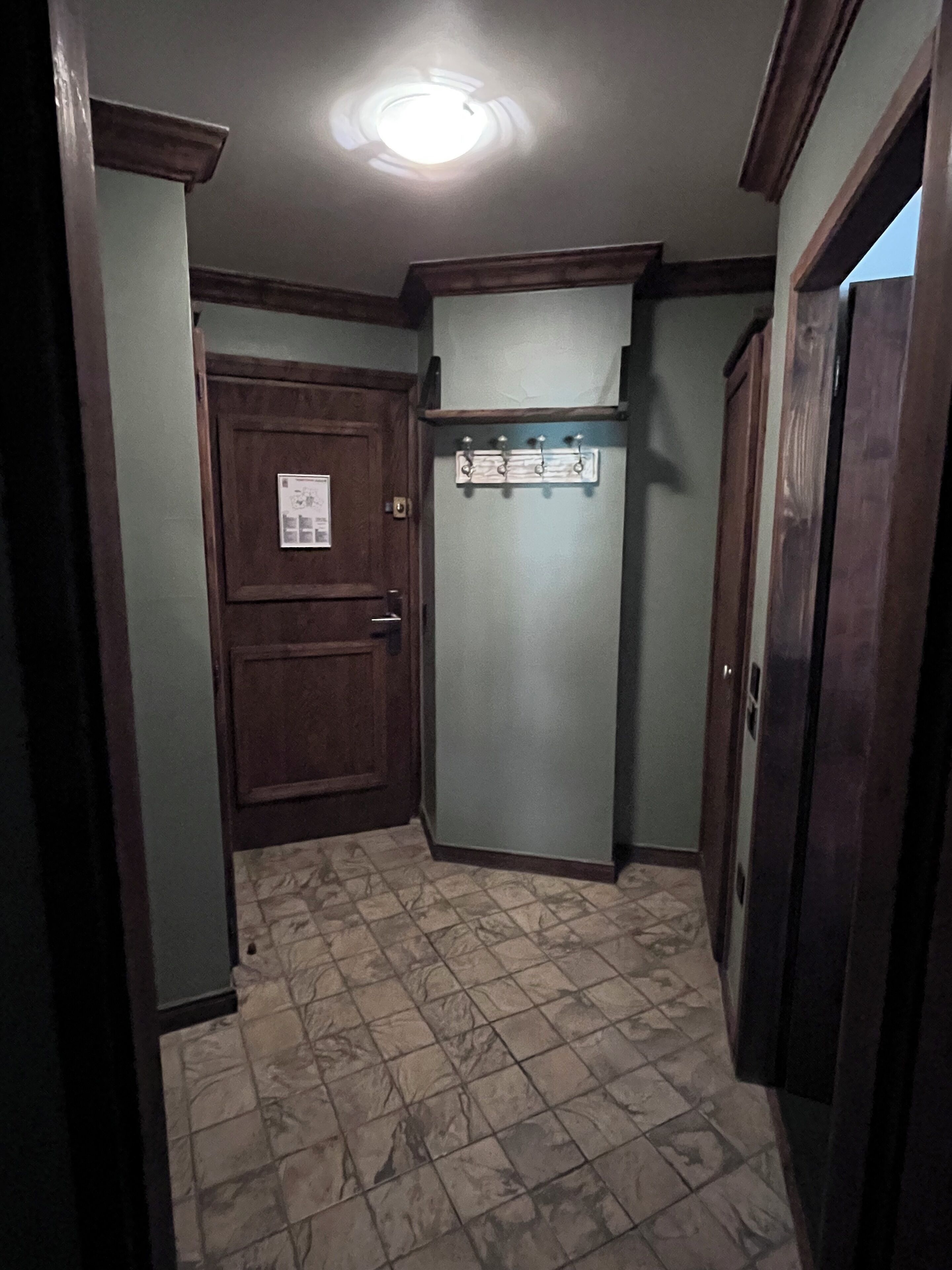 A narrow hallway with a wooden door, a coat rack, and a tiled floor.