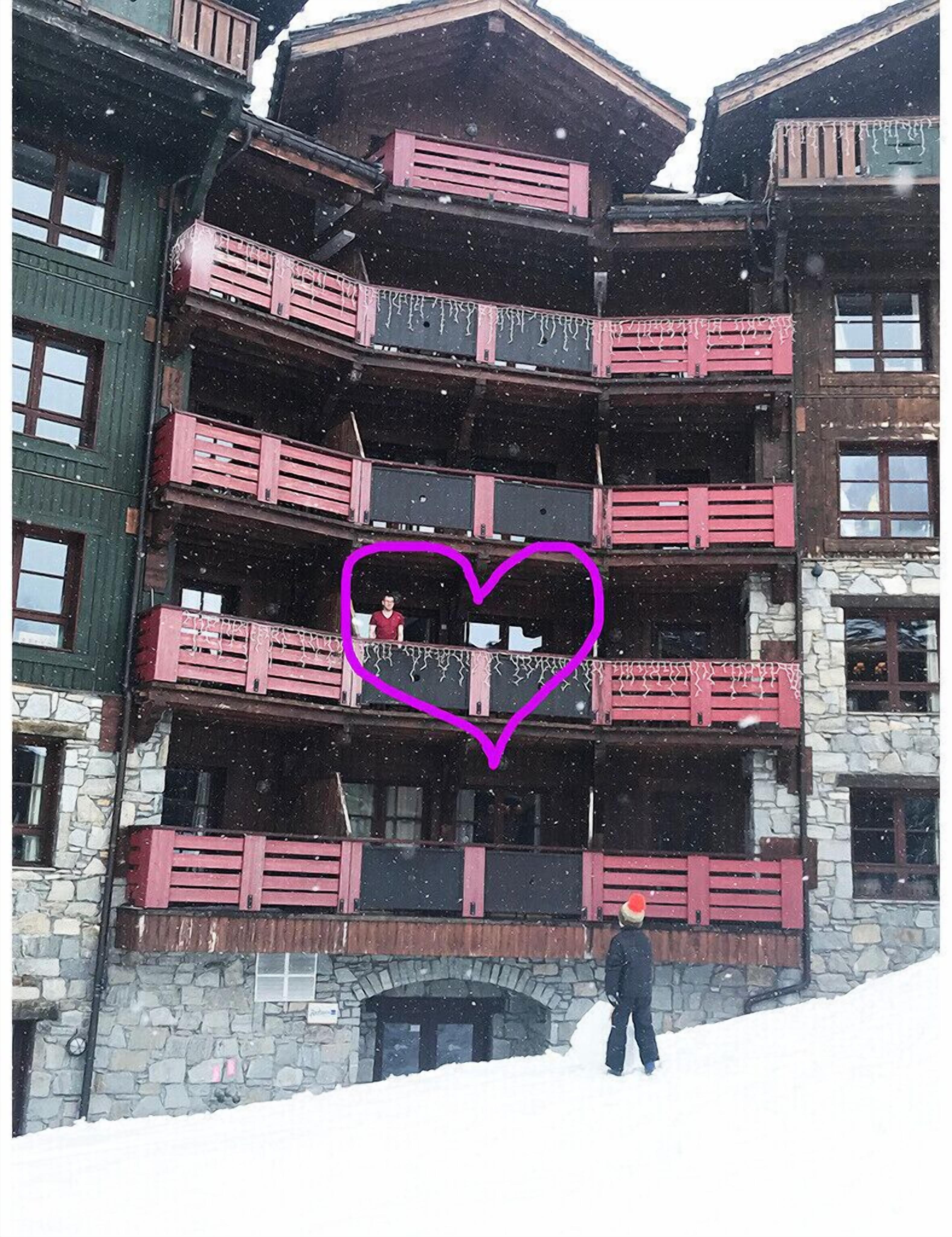 A multi-story building with balconies, stone walls, and a person standing in the snow.