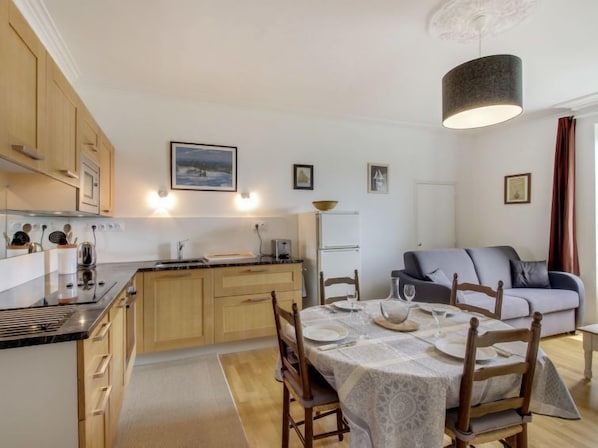 Cozy living space with a kitchen and dining area, featuring a sofa and wooden chairs.