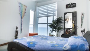 A bedroom with a bed, a window with blinds, a plant, a mirror, and a wall decoration. - EDIFICIO POSIEDON located in the exclusive area of Laugito (Cartagena)