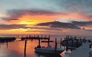 Un puerto deportivo con barcos amarrados, un muelle que se adentra en el agua y una puesta de sol con nubes en el cielo.