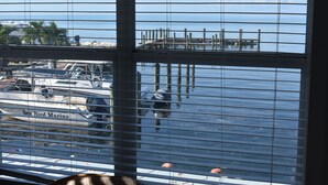 Een jachthaven met aan wal liggende boten, een steiger die het water in reikt, en een uitzicht door jaloezieën.