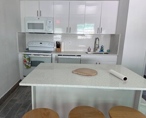 Una cocina con armarios blancos, microondas, estufa y pileta.