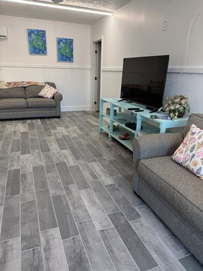 A living room with grey sofas, a flat-screen TV, a light blue coffee table, and artwork on the wall.
