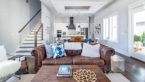 A spacious living room with a brown leather sofa, a wooden coffee table, and a staircase leading to an upper floor.