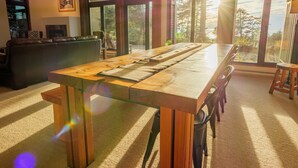 A spacious room with a large wooden table, a leather sofa, and a view of the outdoors through large windows. - Goin'Left - Large 3br Retreat with Spectacular Ocean Views (Ucluelet)