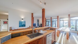 A modern kitchen with a wooden countertop, stainless steel sink, and a dishwasher. There is a large window providing natural light and a view of the outdoors. - Goin'Left - Large 3br Retreat with Spectacular Ocean Views (Ucluelet)