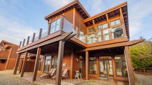 A modern two-story building with a wooden facade, large windows, and a covered outdoor seating area with chairs. - Goin'Left - Large 3br Retreat with Spectacular Ocean Views (Ucluelet)