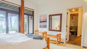 A bedroom with a large bed, wooden chairs, a painting, and a bathroom visible through an open door. - Goin'Left - Large 3br Retreat with Spectacular Ocean Views (Ucluelet)