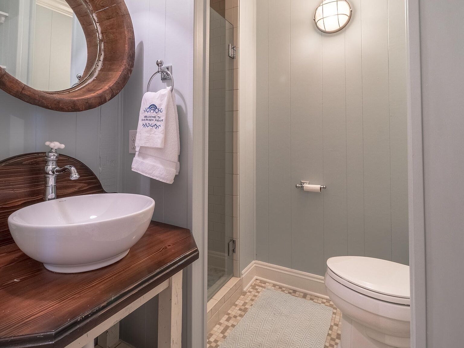 A bathroom with a wooden vanity, a white sink, a towel with a message, a toilet, and a shower area.