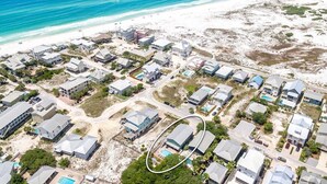 Vista aérea de uma área residencial costeira com casas, uma praia e um oceano azul e límpido.