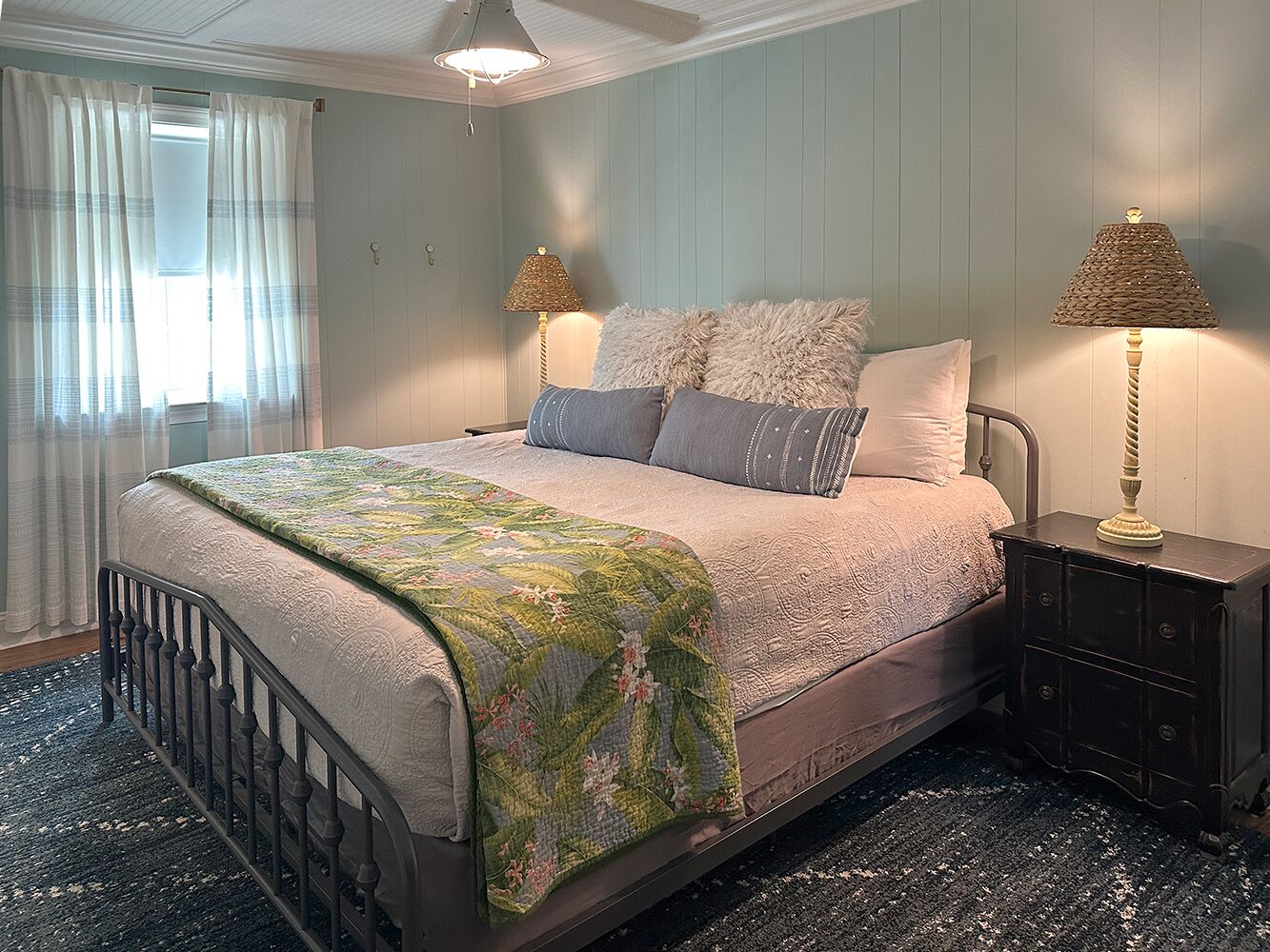 A bedroom with a bed, two bedside tables, a window with curtains, and a ceiling fan.