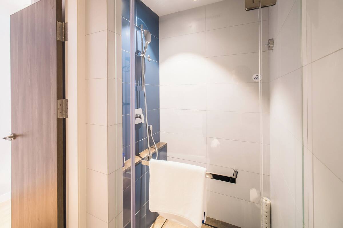 A modern bathroom with a glass shower enclosure, a wooden door, and a white toilet.