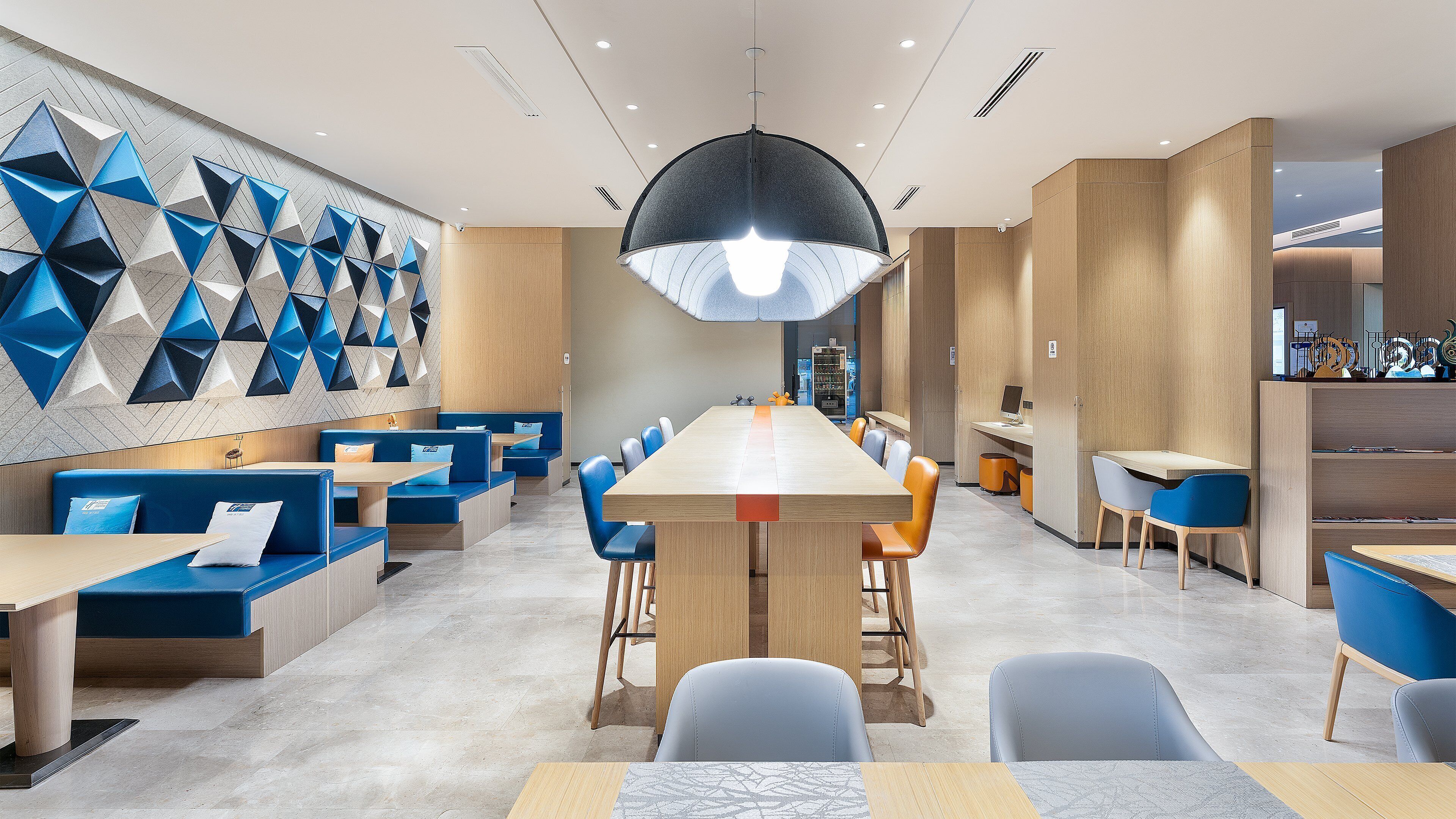 Ein modernes Restaurant mit einem langen Gemeinschaftstisch, blauen Sitzgelegenheiten und geometrischen Wandverzierungen.
