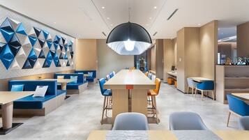 Ein modernes Restaurant mit einem langen Gemeinschaftstisch, blauen Sitzgelegenheiten und geometrischen Wandverzierungen.