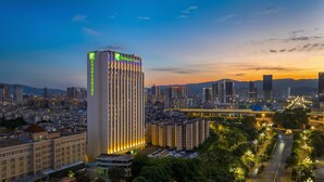 Un hotel moderno de gran altura con señalización iluminada, rodeado por un paisaje urbano con edificios densos y un puente al fondo.