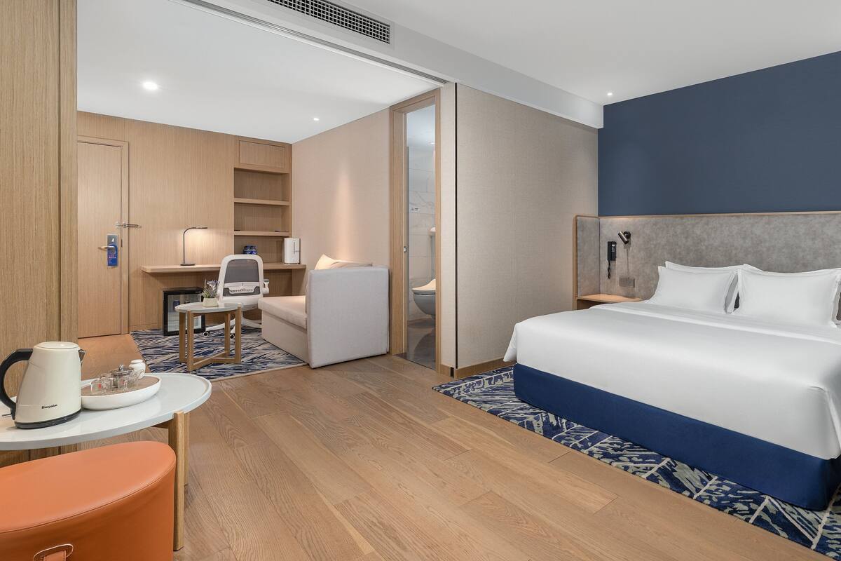 A hotel room with a bed, bedside table, chair, desk, and a bathroom visible through an open door.