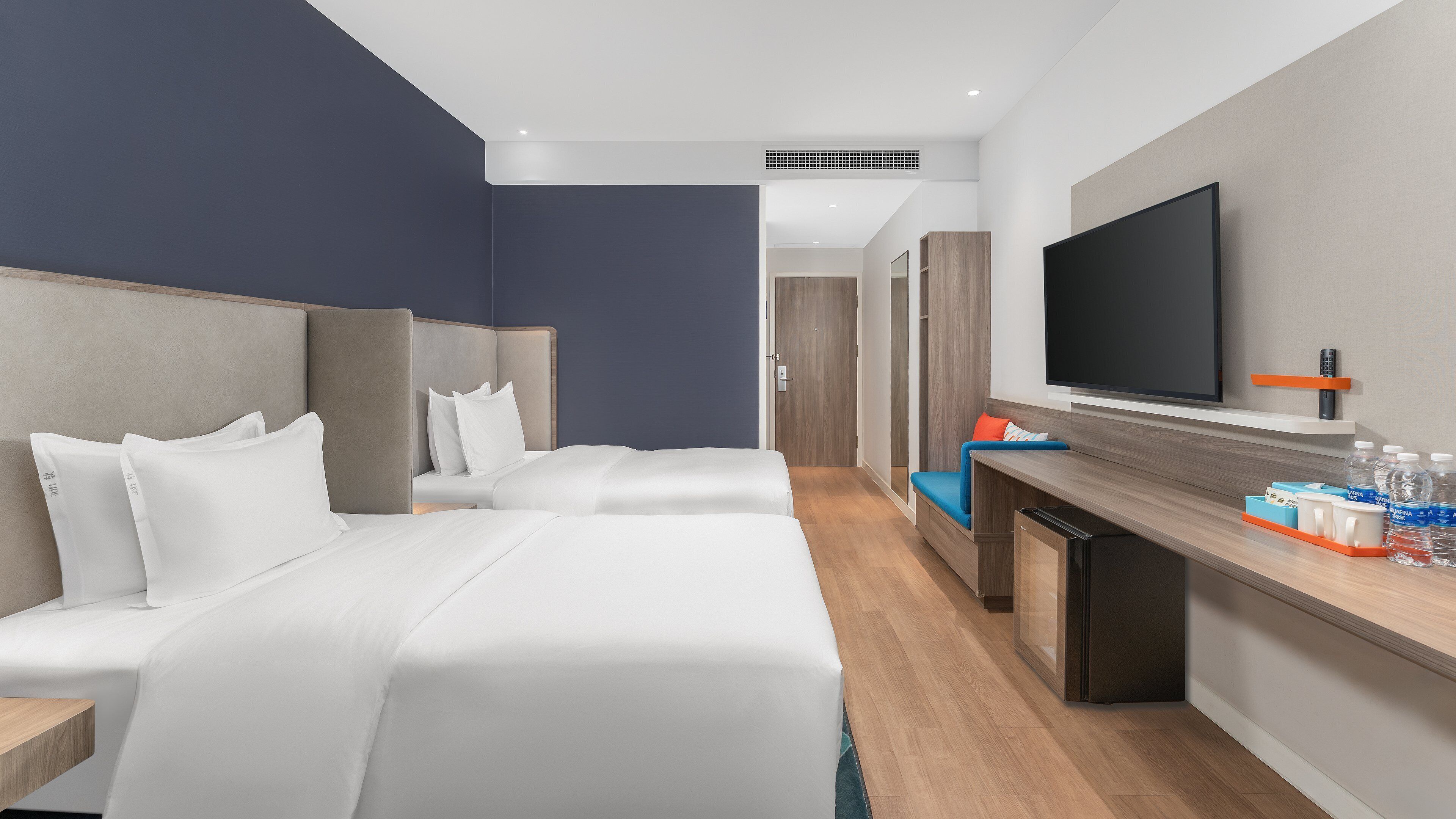 A hotel room with two beds, a desk, a TV, and a minibar.