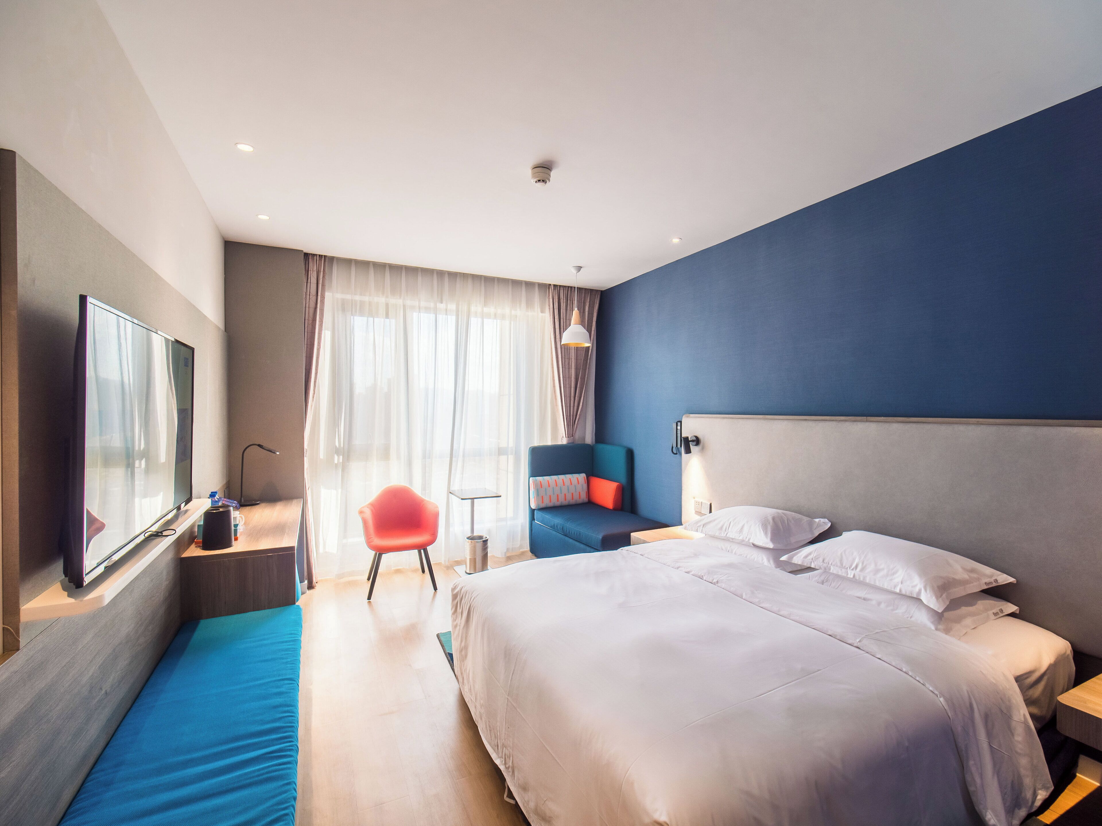 Une chambre d’hôtel moderne avec un grand lit, un coin salon avec un fauteuil, une télévision et une petite table.