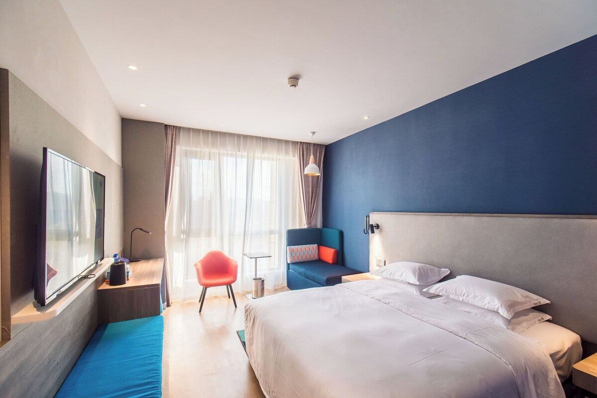 Una camera d'albergo moderna con un letto grande, una zona salotto con una poltrona, una TV e un tavolino.
