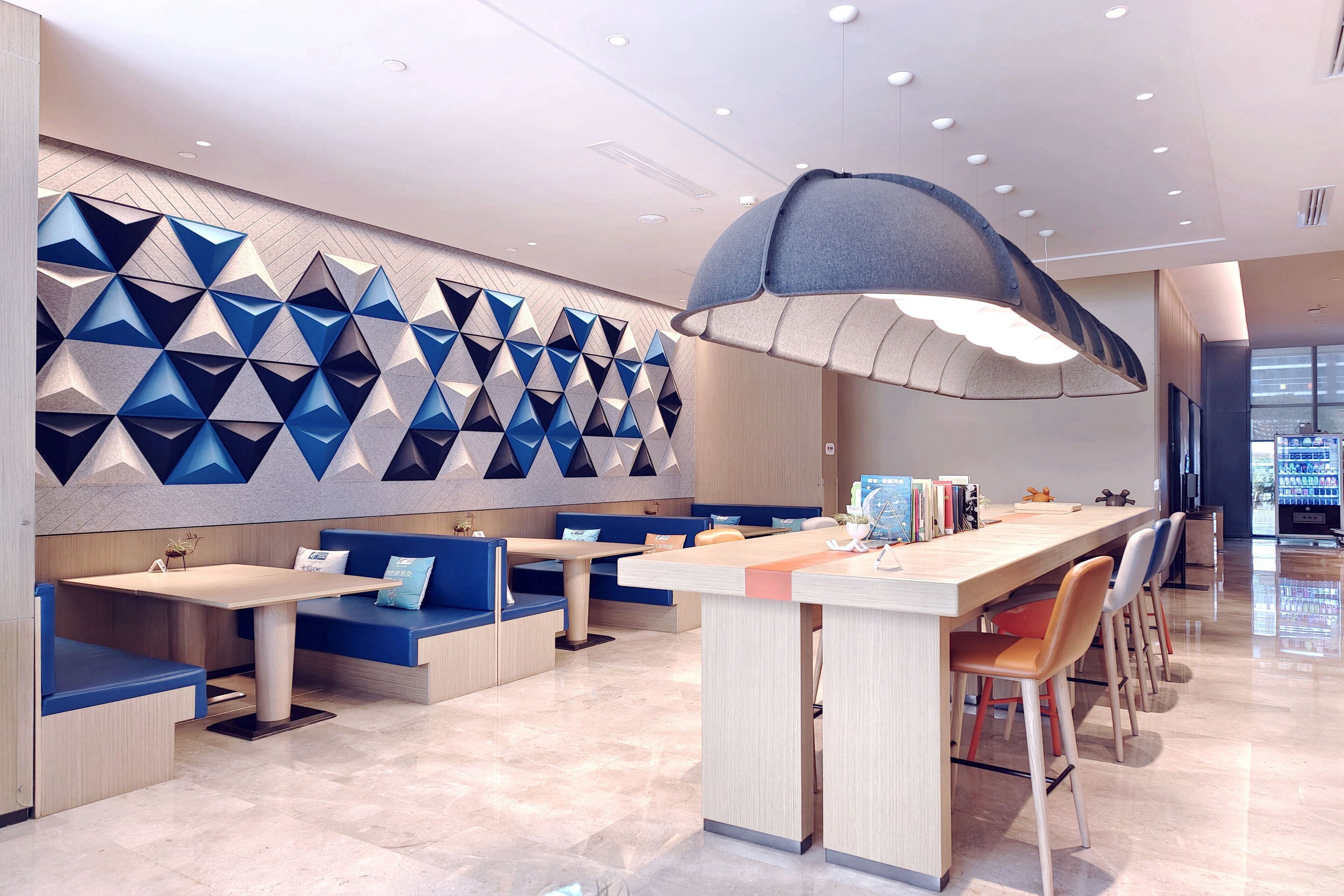 A modern restaurant with a long counter, blue seating, and a geometric wall design.