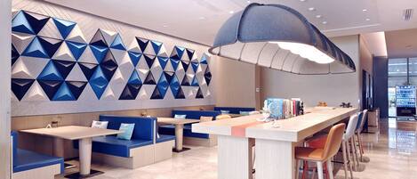 A modern restaurant with a long counter, blue seating, and a geometric wall design.