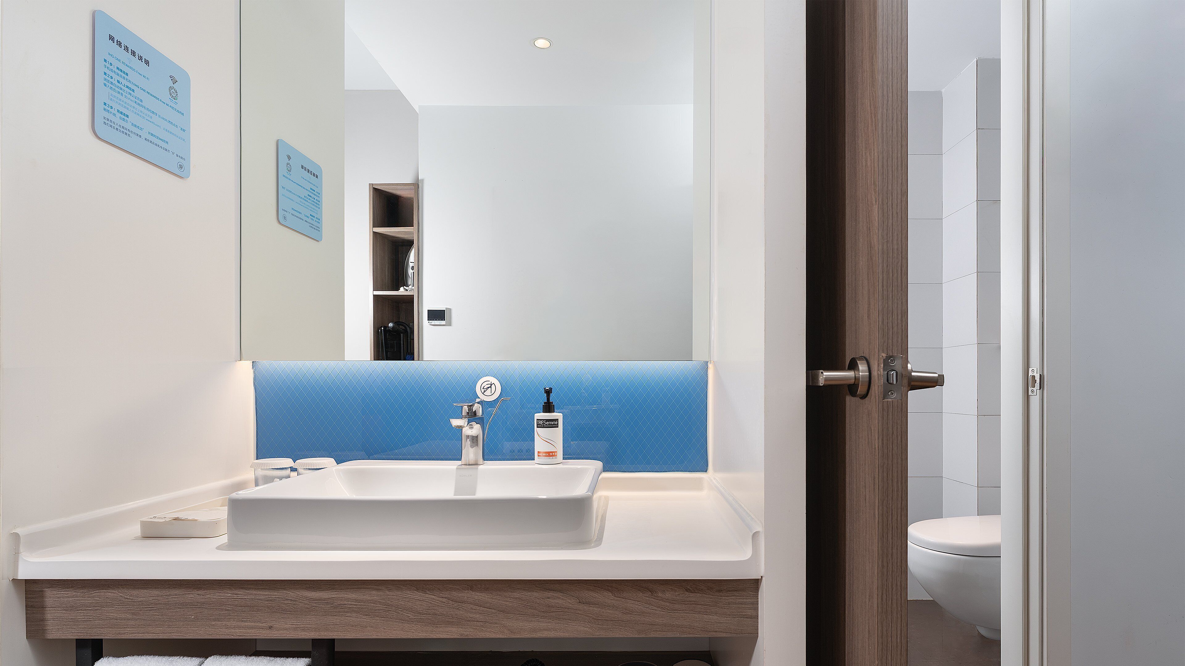 Un bagno moderno con un lavandino bianco, uno schienale piastrellato in blu e un mobile contenitore in legno.