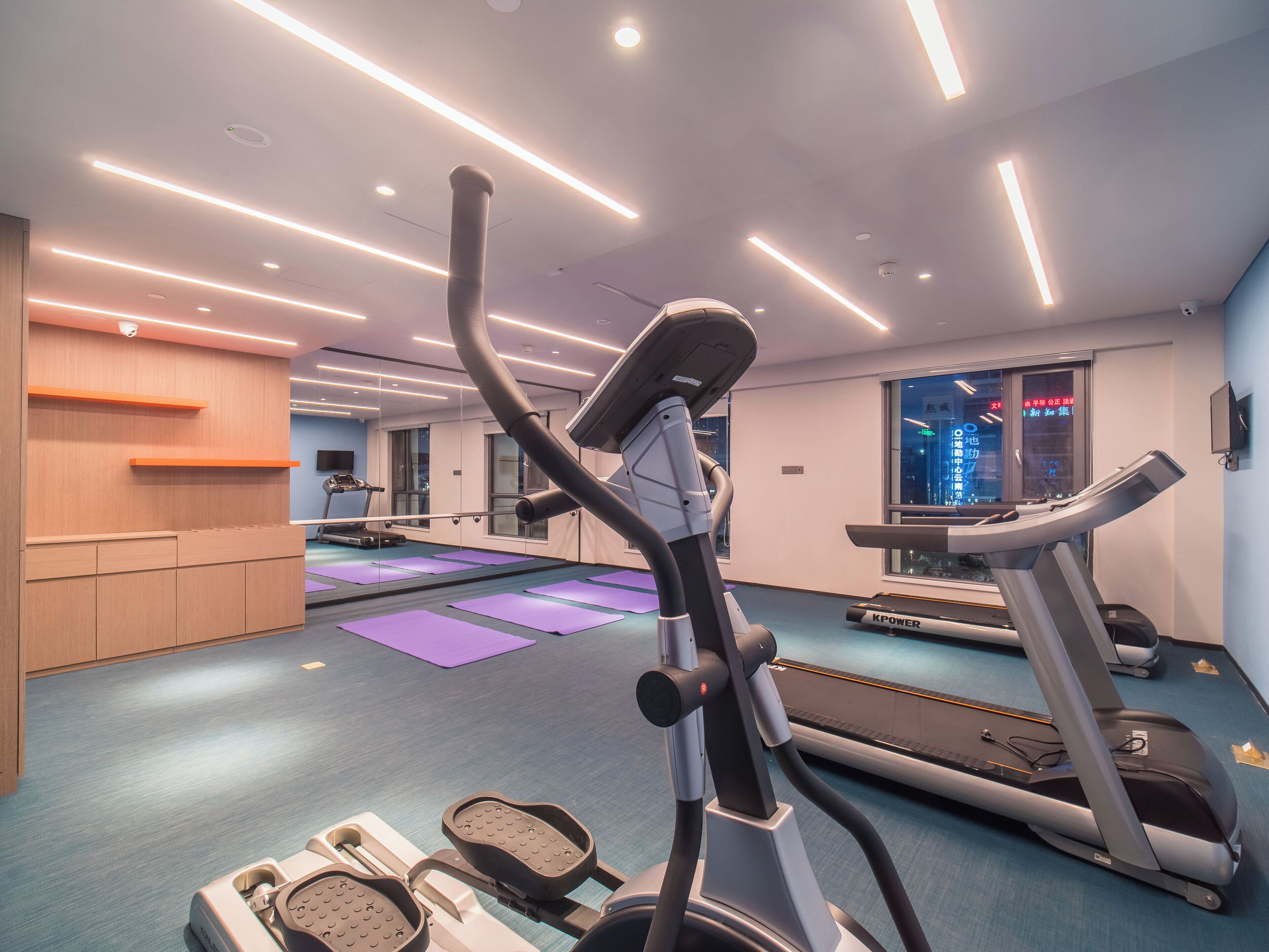 Een sportschool met loopbanden, elliptische trainers en een spiegelwand.