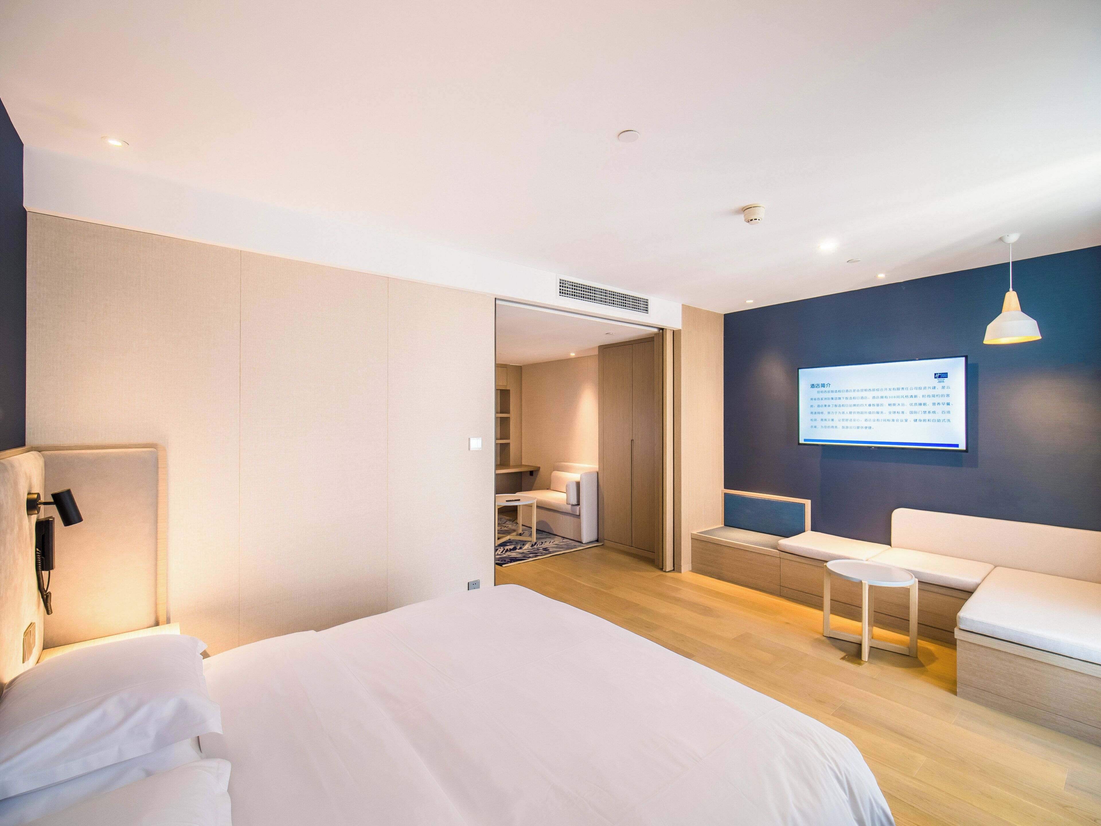 Et moderne hotelværelse med seng, natbord og et siddeområde med et lille bord og bænk.
