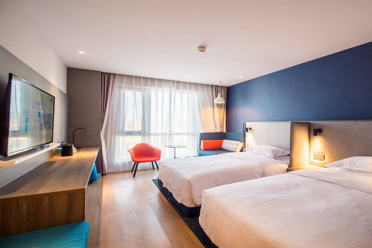 A hotel room with two beds, a TV, a desk, and a chair.