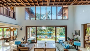 A spacious living area with a high ceiling, large windows, and a view of a lush garden. - Villa Rusa Biru - Peaceful Ricefield Views in Central Canggu (Kecamatan Kuta Utara)