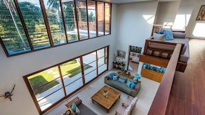 A spacious living area with a large window, a sofa set, a coffee table, and a wooden bench. - Villa Rusa Biru - Peaceful Ricefield Views in Central Canggu (Kecamatan Kuta Utara)