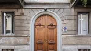 Una puerta doble de madera con arco superior, flanqueada por muros de piedra y ventanas.