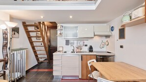 Cocina compacta con escalera de madera, comedor con mesa y sillas, y kitchenette con microondas y hervidor.
