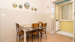 A dining area with a tiled wall, a table with a patterned tablecloth, four chairs, and a window with a view of the outside. - Ritamar by Interhome (Sorrento)