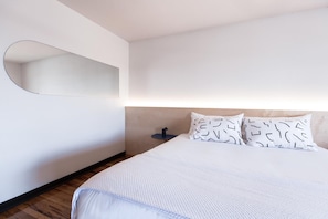 A modern hotel room with a large bed, a round mirror on the wall, and a small bedside table with a lamp. - The Iris Motel (Nashville)