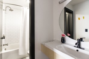 A modern bathroom with a white bathtub, a large mirror, and a sink with a black faucet. - The Iris Motel (Nashville)