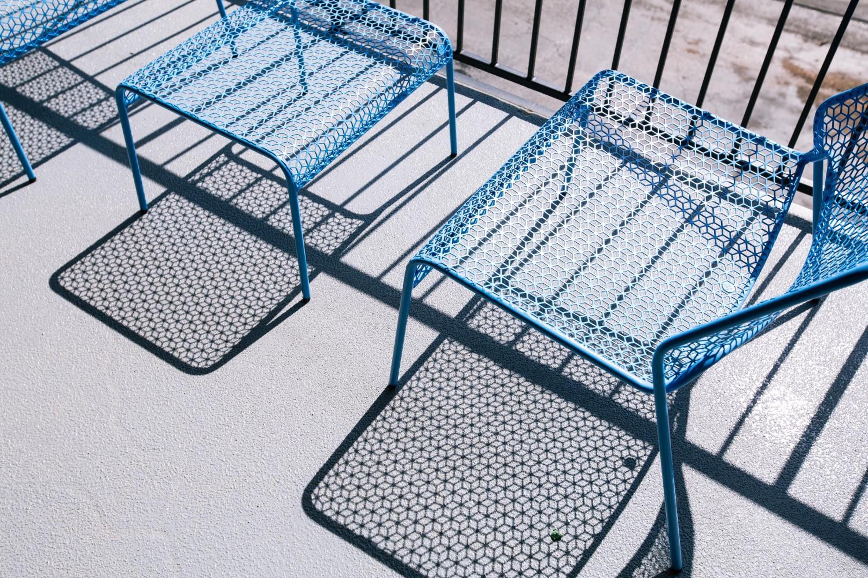 A row of blue metal chairs with a hexagonal pattern on the seat and backrest, arranged on a concrete surface.
