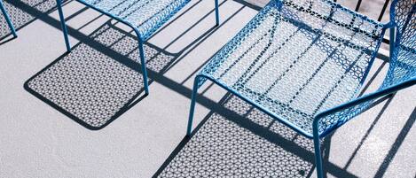 A row of blue metal chairs with a hexagonal pattern on the seat and backrest, arranged on a concrete surface.
