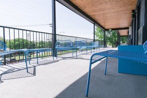 An outdoor seating area with blue metal chairs and tables, a covered roof, and a view of the street and greenery. - The Iris Motel (Nashville)