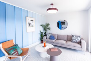 A modern living room with a blue and white color scheme, a round mirror, a sofa with patterned cushions, a coffee table, and a chair with a colorful cushion. - The Iris Motel (Nashville)