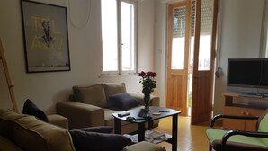 A living room with a sofa, a coffee table with a book and remote, a TV, and a door leading outside. - Specious room next to the beach (Tel Aviv-Yafo)