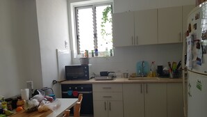 A compact kitchen with a microwave, toaster, and sink. There is a window with plants visible outside. - Specious room next to the beach (Tel Aviv-Yafo)