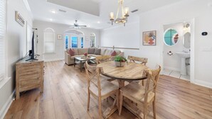 A spacious living room with a wooden dining table, a sofa, and a ceiling fan. - Pier Park only 50 Steps to the beach! Pet friendly. Ocean View.  (Panama City Beach)