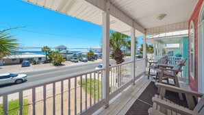 A covered porch with a view of a street and buildings, featuring a railing and a bench. - Pier Park only 50 Steps to the beach! Pet friendly. Ocean View.  (Panama City Beach)
