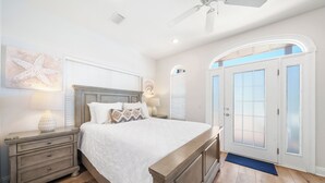 A bedroom with a bed, nightstands, a ceiling fan, a window with blinds, and a door with frosted glass panels. - Pier Park only 50 Steps to the beach! Pet friendly. Ocean View.  (Panama City Beach)